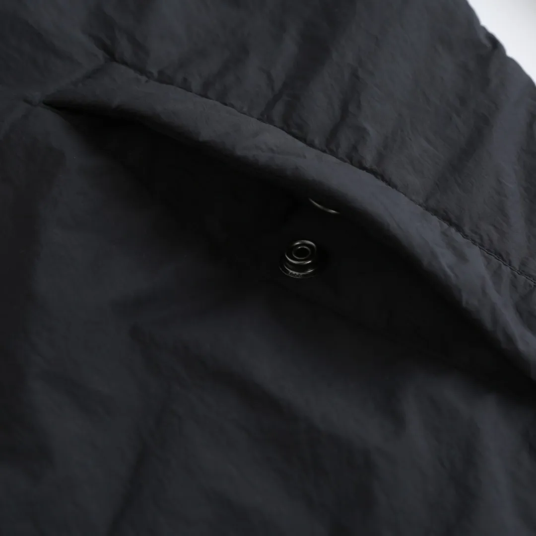 🅿️680 Ralph Lauren pony embroidered light cotton jacket. The fabric is made of high-density nylon taffeta fabric, which combines pragmatism and classic texture. The density is about 210T-300T, the surface is smooth and slightly matte, it has excellent windproof and waterproof performance (with DWR water-repellent treatment), it has strong wrinkle resistance and is easy to care for, which is in line with the positioning of American casual "durable and practical". Classic dark black, using vat dyeing process (dye penetrates into the fiber), the color fastness reaches ISO level 4 or above, preventing fading or color transfer after washing. The lining is made of light cotton-polyester blended fabric (65% Polyester + 35% Cotton) to reduce the friction between the fabric and the inner clothing and improve the smoothness of wearing; the blended material has both breathability and durability to avoid the stuffy feeling of pure nylon lining. The style is a loose fit of the classic Coach Jacket, with slightly dropped shoulder lines (shoulder width is 1-2cm wider than the standard fit). The length reaches the hips, and the sleeves are slightly tapered straight sleeves, taking into account both freedom of movement and casual style. The Polo horse logo on the left chest is flat satin stitch embroidered (satin embroidery), embroidery thread: 100% polyester high color fastness embroidery thread (the color number is consistent with the brand’s standard red color card), the stitch density is 12-15 stitches/cm, the outline of the horse logo is clear, and the details of the rider and horse are burr-free. The embroidery is positioned accurately through the template (12cm from the bottom of the neckline and 8cm from the placket) to ensure left-right symmetry and centering. The seams of the body are made of double-needle flat seams (needle pitch 3cm/10 needles), the stitches are flat and straight, the stitching color is dark black (the same color as the fabric), and the stitch width is 0.5cm, which enhances firmness while forming simple decorative lines. The front placket is spliced ​​with the body. The placket is made of double-layer folding + flat seam splicing. The thickness is about 0.3cm to ensure that the buttons are not easily deformed when fixed. The edges of the placket are cut with a hot knife to avoid burrs. The armholes where the sleeves and body are joined are made with round-head keyhole machine seams + flat seams. After the splicing, the armholes have a natural curvature and no sense of tightness during movement. The height of the sleeves is about 8-10cm, which is in line with the loose characteristics of casual jackets. The main buttons are made of black urea resin buttons with a matte surface. The buttonholes are hand-made keyholes (6 strands of cotton thread, keyhole density of 8 stitches/mm), and the edges of the eyelets are smooth and without burrs. The first button on the neckline is a hidden button (diameter 12mm), which prevents the neckline from opening and improves the neatness of wearing. Size:S-M-L-XL